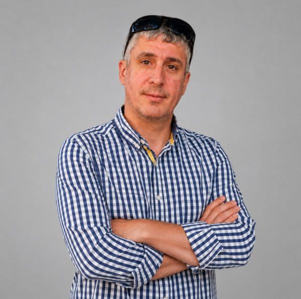 Portret al lui Ionuț Pepenar purtând o cămașă în dungi albastre, cu o bibliotecă în fundal.